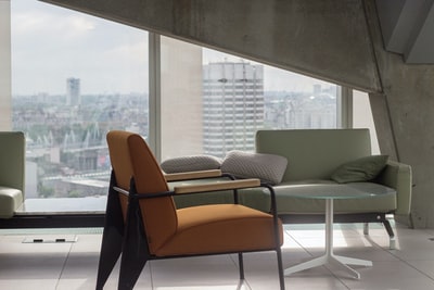 橙色织物软垫扶手椅，黑色金属底座，靠近圆形透明玻璃顶桌和灰色沙发